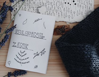 Picture with a folded white paper booklet with 'coloring zine' on the cover